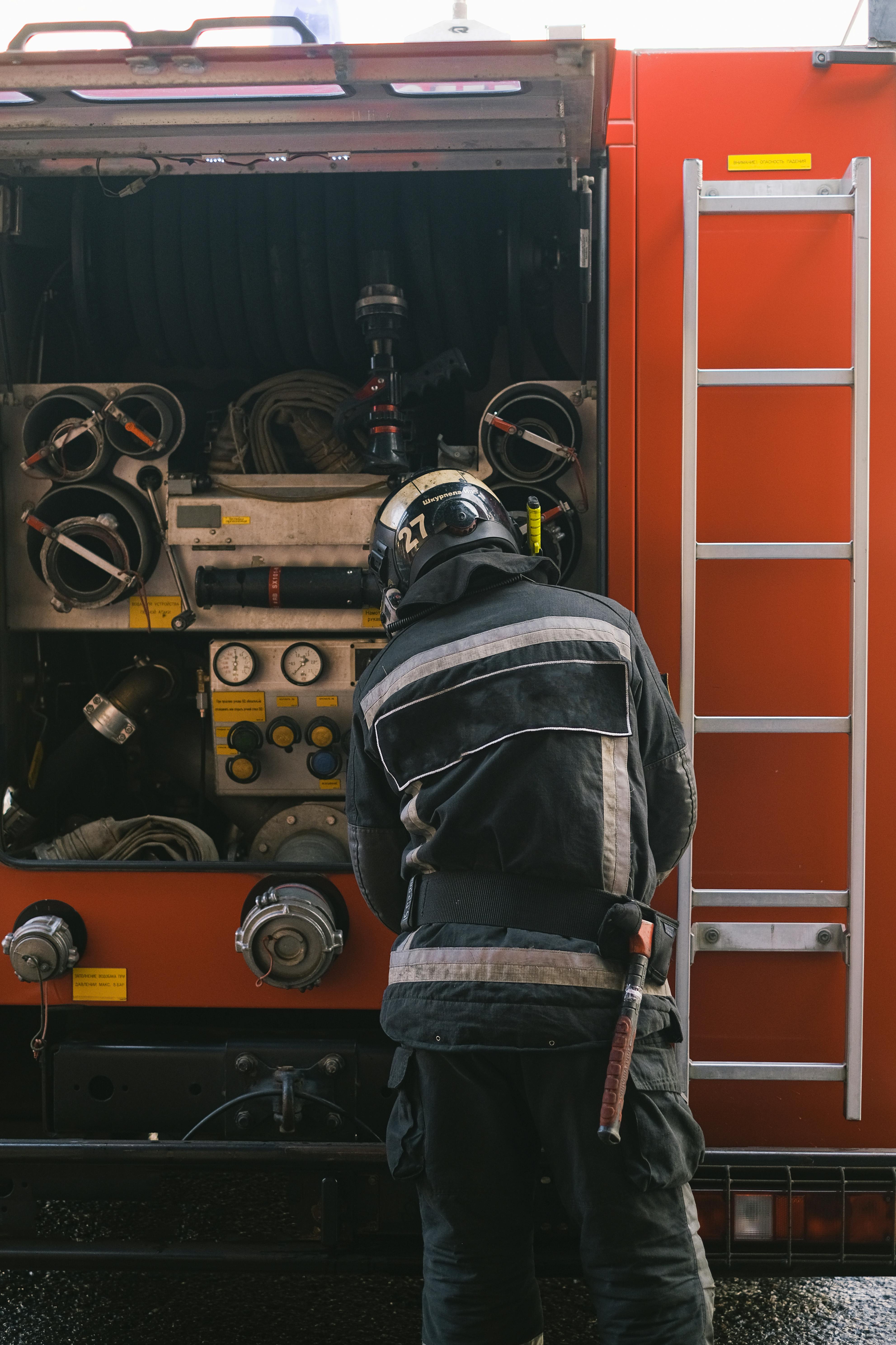 Firefighter examining equipment on a firetruck with open compartment.